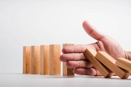 Stopping the domino effect. Business crisis management. Close-up hand interfering collapsing wooden dominoes on white background. Business strategy and successful intervention. Risk protection.